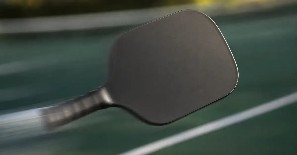Pickleball paddle in motion, blurred handle and sharp paddle face over a blurred green court