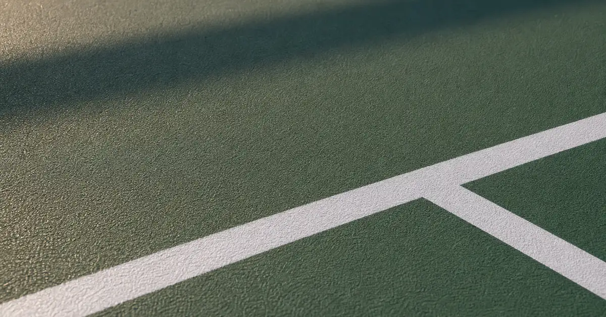 Close-up abstract photograph of an outdoor pickleball court surface texture at the kitchen line
